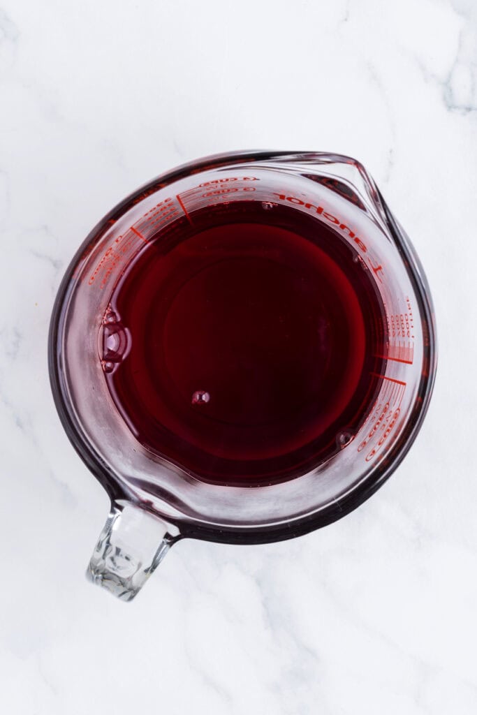 Measuring cup filled with deep red cherry jello liquid seen from above