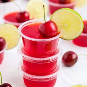 Square crop of jello shots stacked and garnished with a cherry and lime wedge