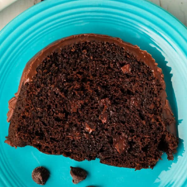 Square crop close-up of a slice of Chocolate Chip Chocolate Bundt Cake on a blue plate, with chocolate chips scattered nearby.