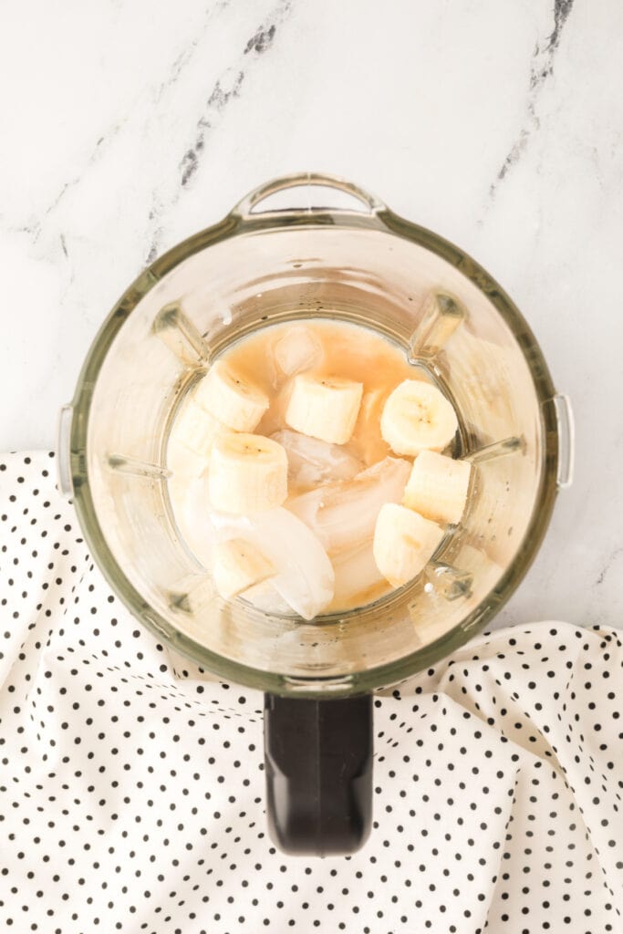 Ice, banana chunks, and cocktail ingredients inside a blender before blending