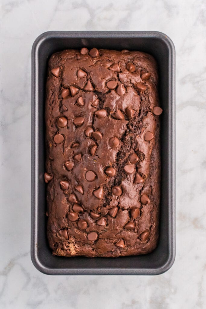 Baked double chocolate zucchini bread loaf in a pan with chocolate chips on top.