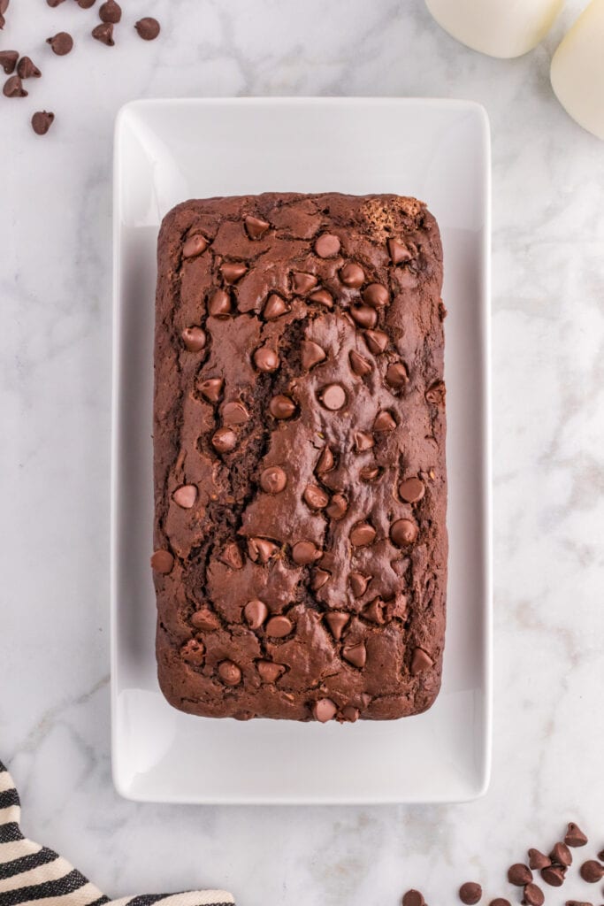 Overhead view of double chocolate zucchini bread on a white platter with chocolate chips scattered around.