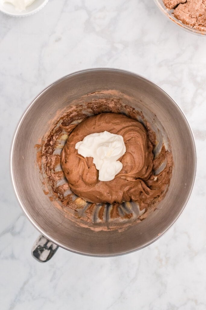 Sour cream being added to the chocolate batter in the mixer bowl.