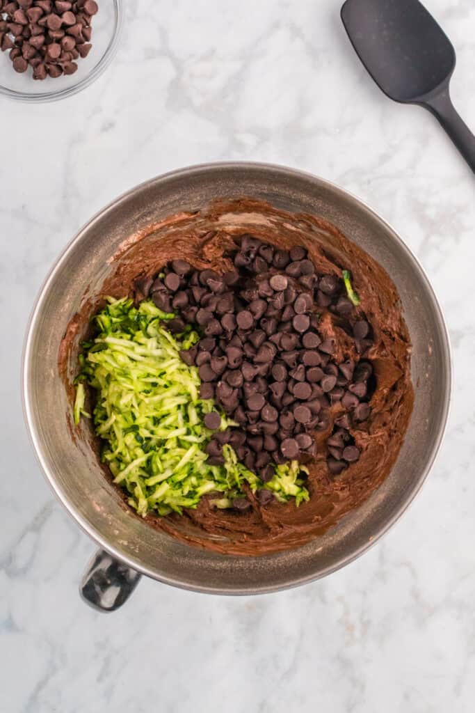 Shredded zucchini and chocolate chips added to chocolate batter in the bowl.