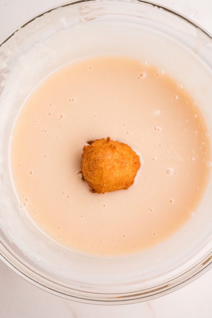 Single donut hole being dipped into vanilla glaze