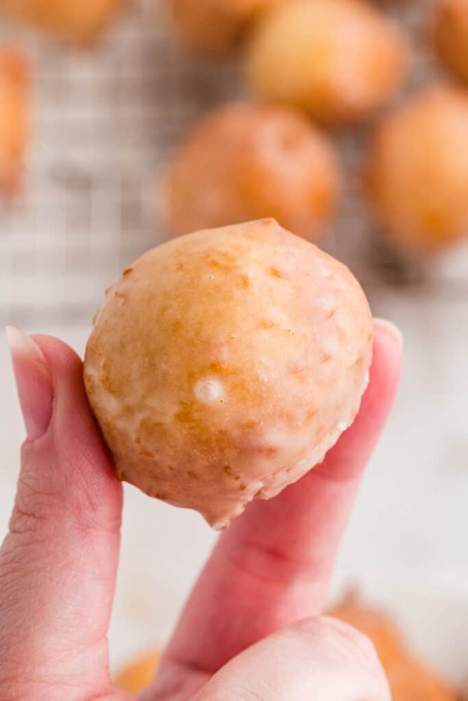 Hand holding a single glazed donut hole close up