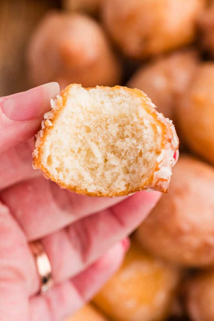 Hand holding a glazed donut hole with a bite taken out, showing the inside