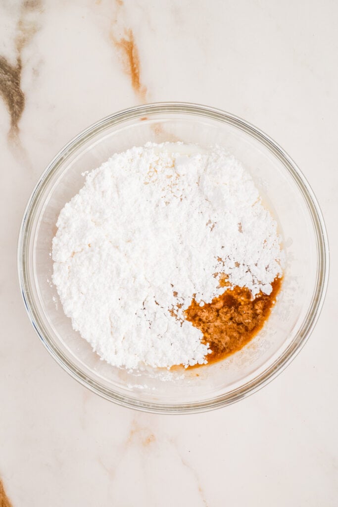 Powdered sugar and vanilla extract added to a bowl for glaze preparation