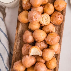 Overhead view of a wooden tray filled with glazed donut holes, some halved