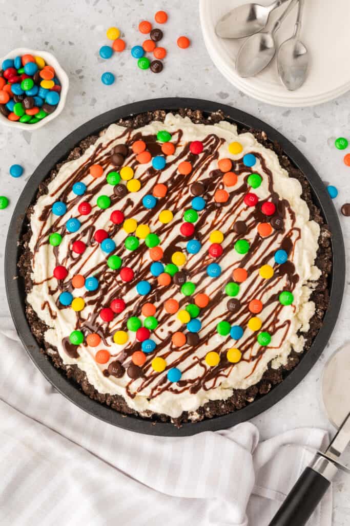 Overhead view of an ice cream pizza topped with M&M's and chocolate drizzle on a black pizza pan