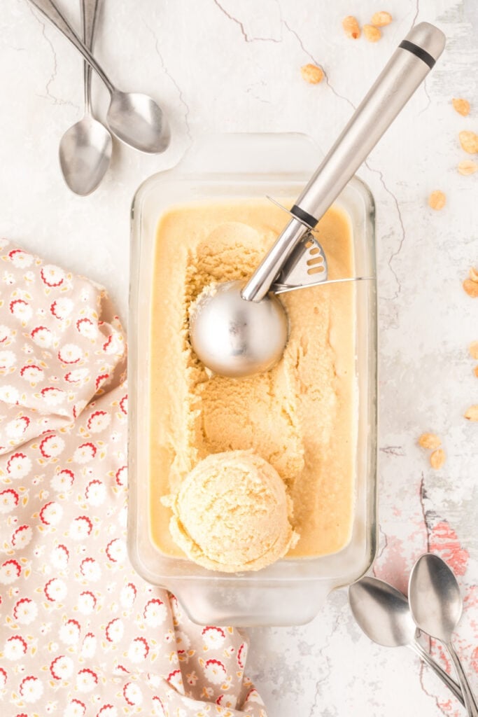	Scooping peanut butter ice cream from a glass container with a metal scoop.