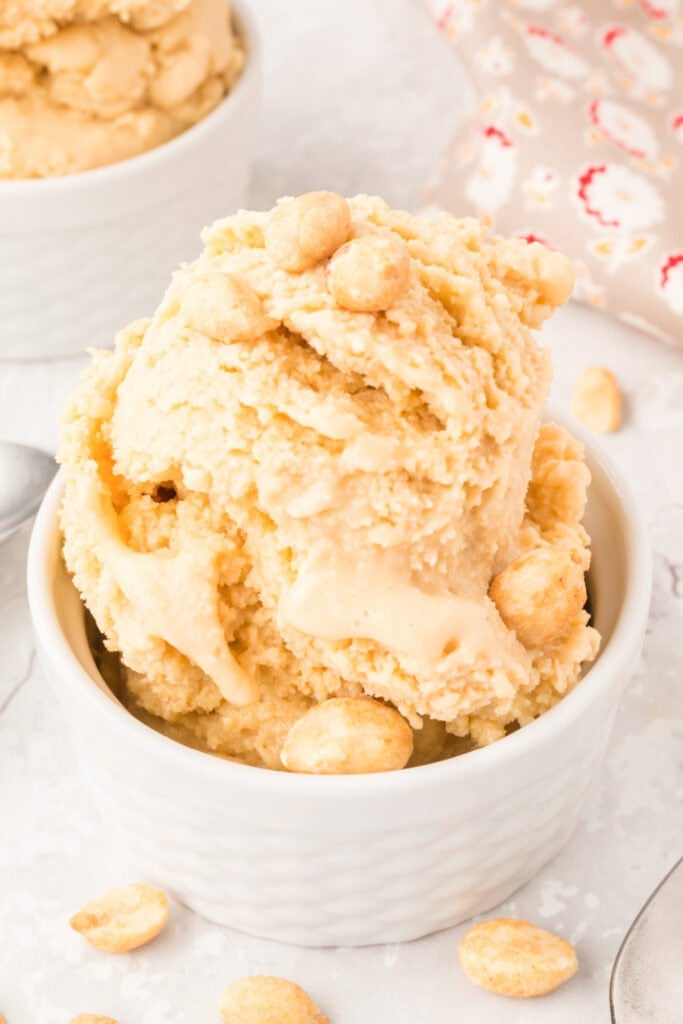Close-up of a scoop of peanut butter ice cream in a ramekin with whole peanuts on top.