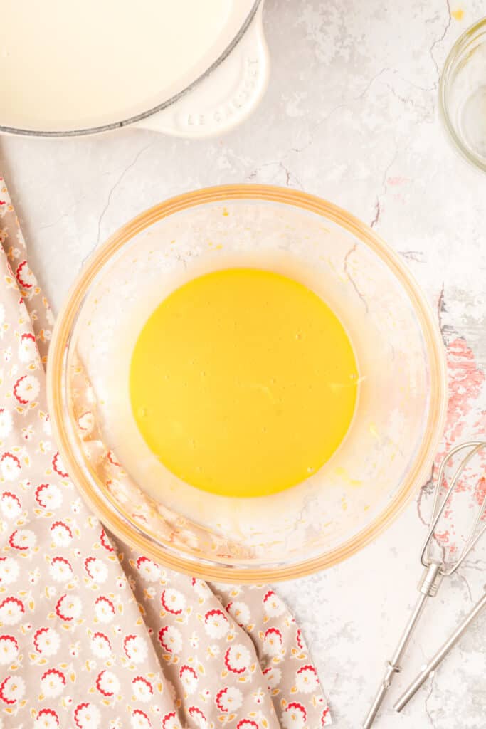 Beaten egg yolks in a clear mixing bowl with a smooth texture and pale yellow color.