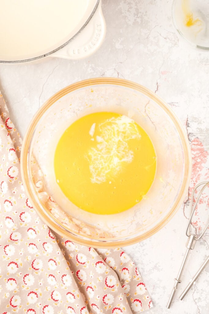 Tempered cream being poured into the egg yolk mixture to combine and thicken the custard base.