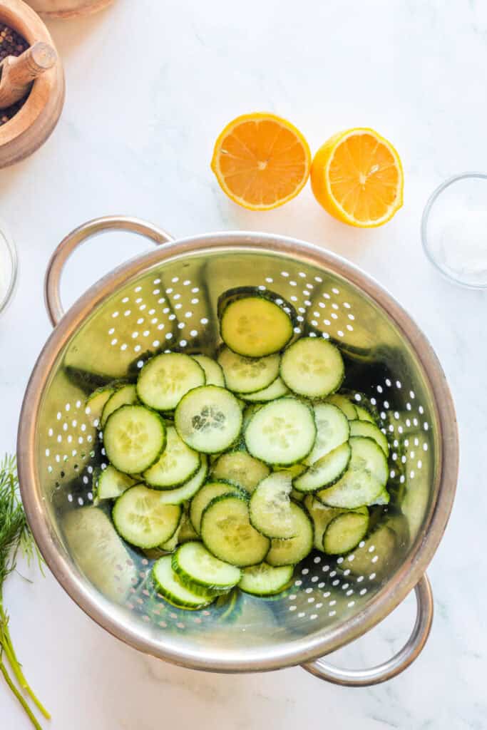 Cucumber slices salted and resting in a stainless steel colander