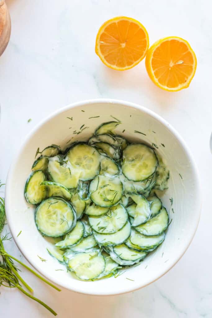 Cucumber salad mixed with creamy dressing and dill in a white bowl