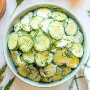 Square crop of cucumber salad with sour cream and dill in a white bowl