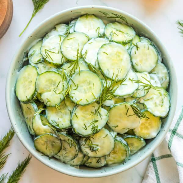 Square crop of cucumber salad with sour cream and dill in a white bowl
