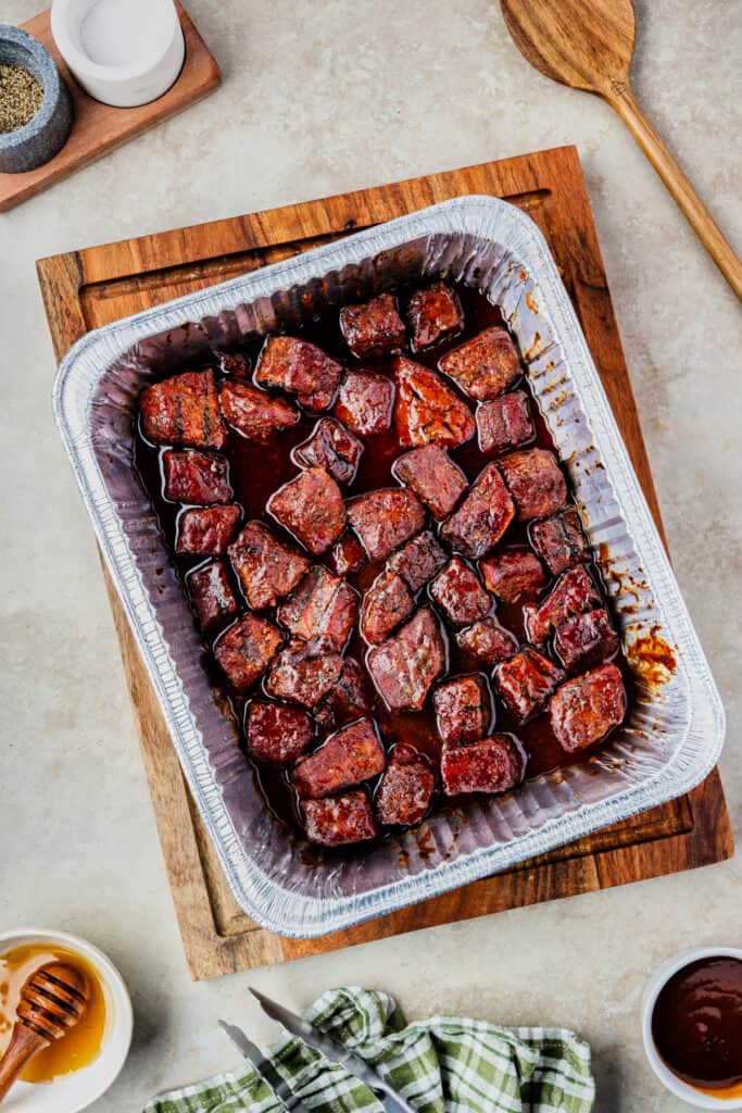 Fully cooked burnt ends in a foil pan, coated in rich, sticky BBQ glaze.