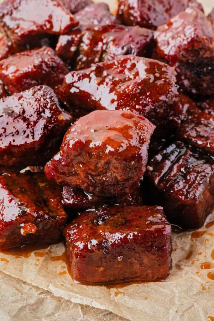 Close-up of saucy Poor Man’s Burnt Ends on parchment paper, glistening with BBQ glaze.