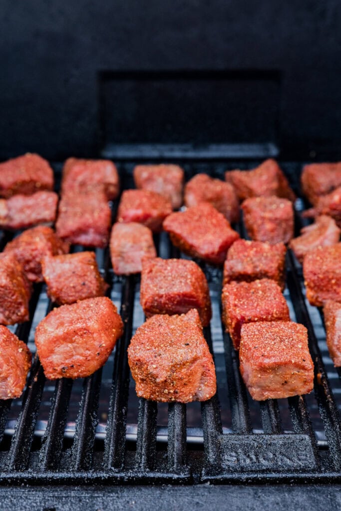 Seasoned chuck roast chunks placed directly on a smoker grill grate.