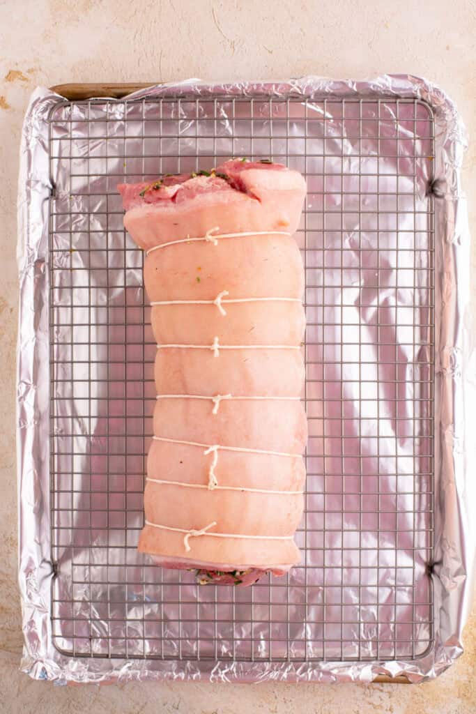 Tied porchetta placed on a wire rack over a foil-lined baking sheet
