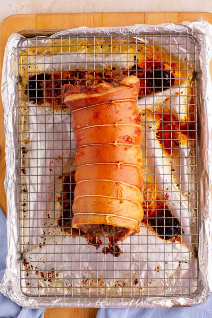 Fully roasted porchetta on a wire rack over a baking sheet, golden and crispy