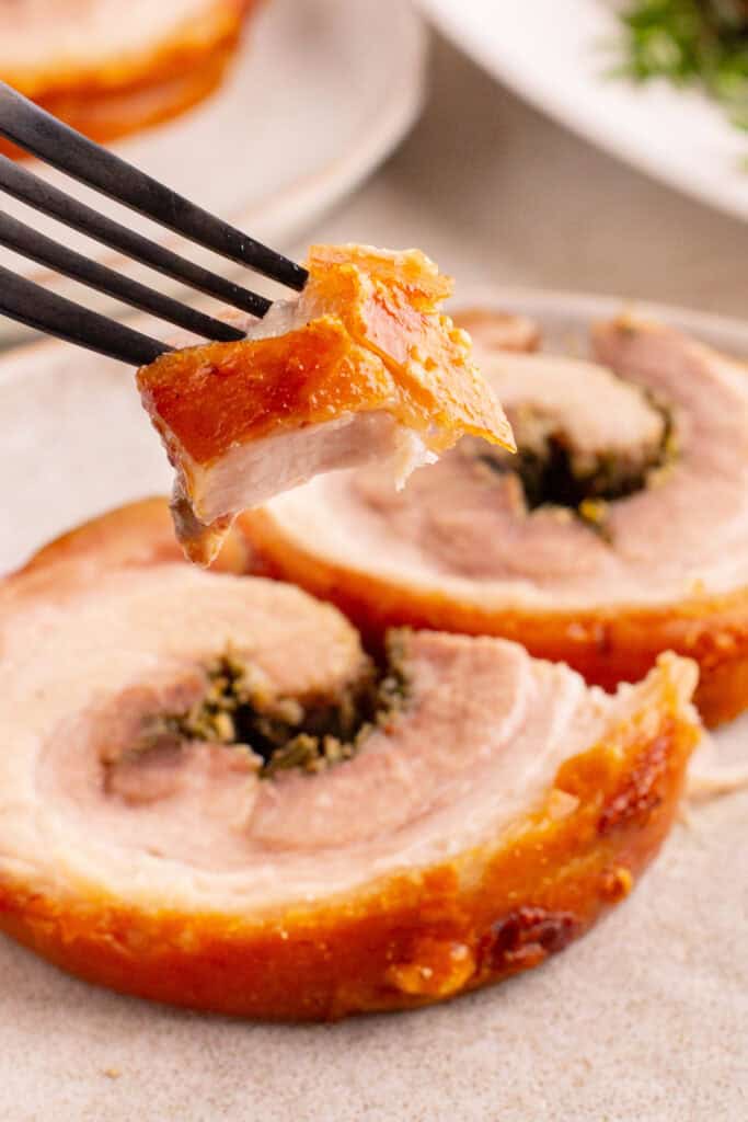 Fork holding a bite of porchetta with crispy skin and juicy meat