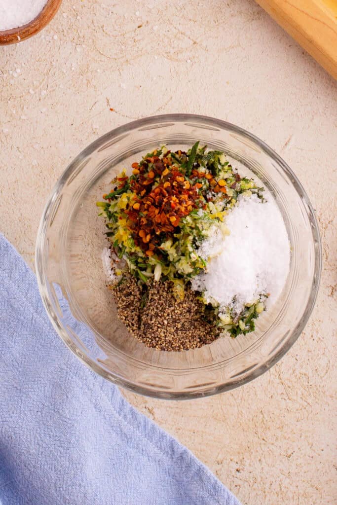 Herb mixture combined with salt, pepper, and red pepper flakes in a bowl