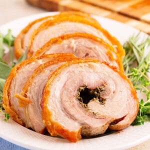 Overhead shot of plated porchetta slices with rosemary and thyme on the side
