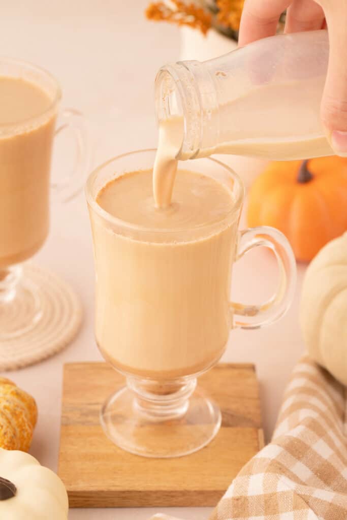 Pumpkin spice creamer being poured into a clear mug with fall decor