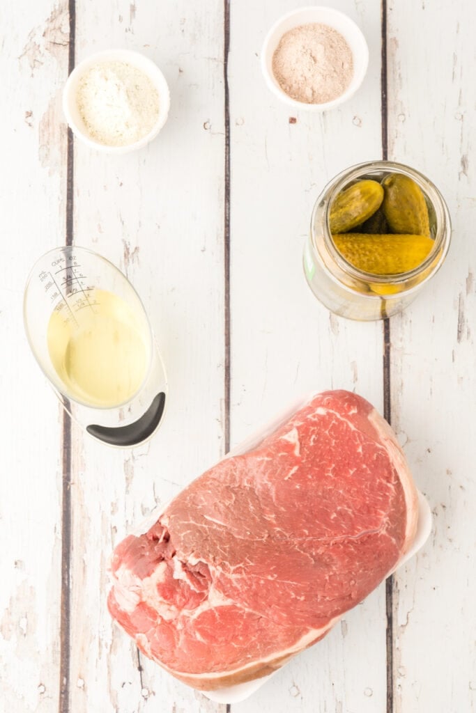 Raw ingredients for dill pickle pot roast: chuck roast, ranch mix, gravy mix, pickles, juice