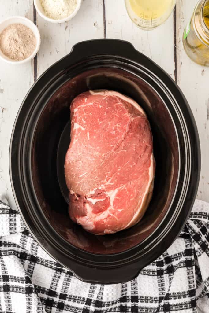 Raw chuck roast placed inside a black slow cooker crock