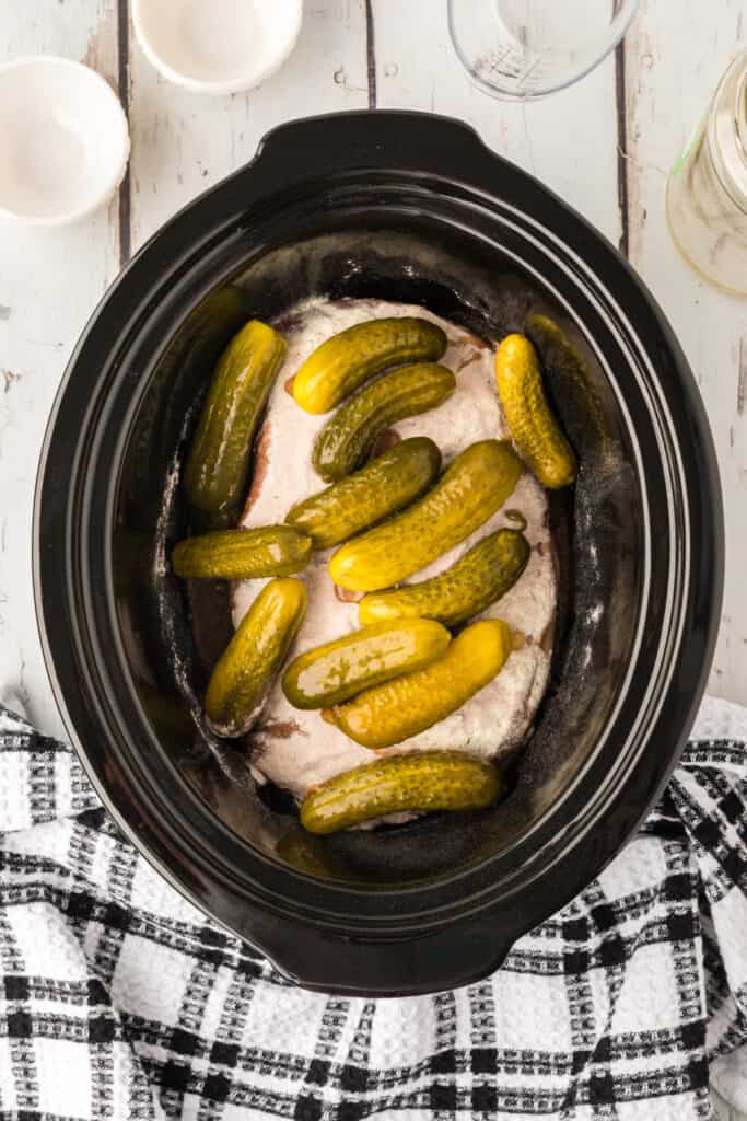 Overhead view of pickles, seasoning, and pickle brine with the roast before cooking