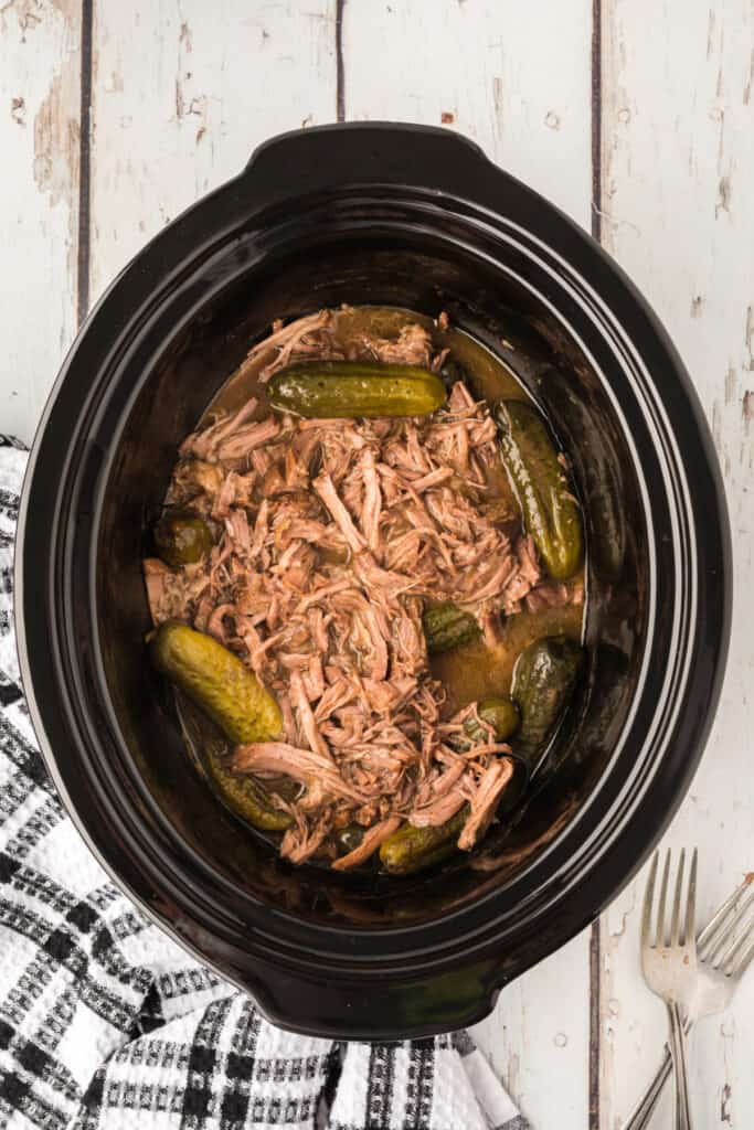 	Shredded dill pickle pot roast with pickles in the slow cooker ready to serve