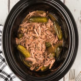 Overhead shot of slow cooker filled with shredded dill pickle pot roast and baby dill pickles