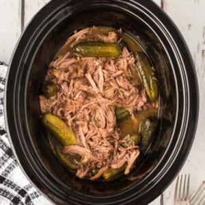 Overhead shot of slow cooker filled with shredded dill pickle pot roast and baby dill pickles