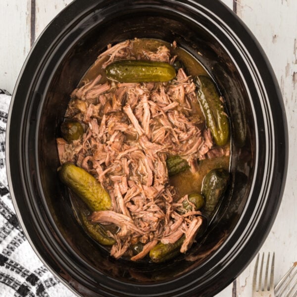 Overhead shot of slow cooker filled with shredded dill pickle pot roast and baby dill pickles