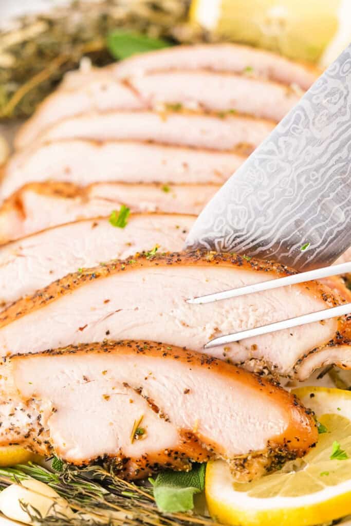 Sliced smoked garlic herb turkey breast being carved with a sharp knife