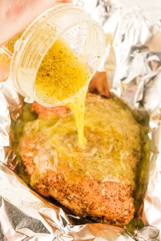 Garlic herb butter being poured over smoked turkey breast in foil