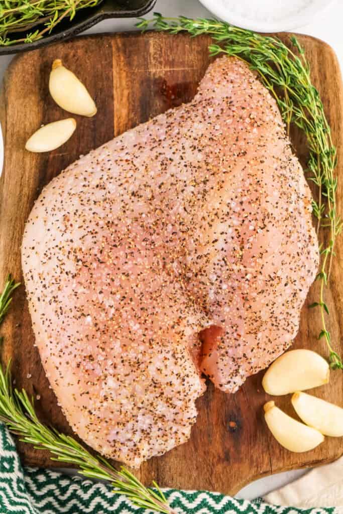 Seasoned raw turkey breast on a cutting board with garlic and herbs