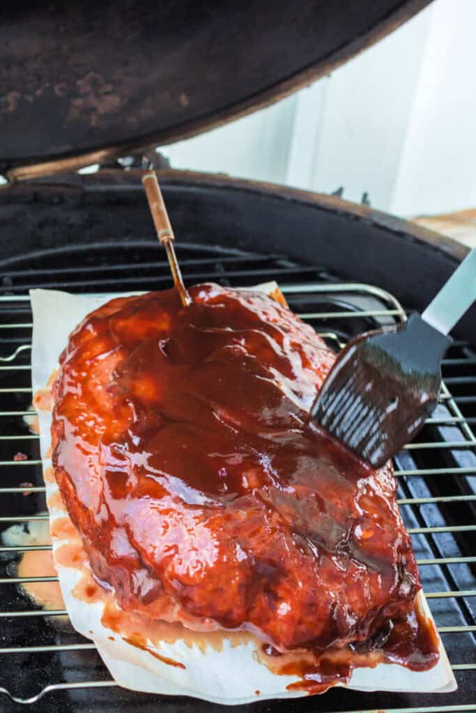 BBQ sauce being brushed over the smoked meatloaf during cooking