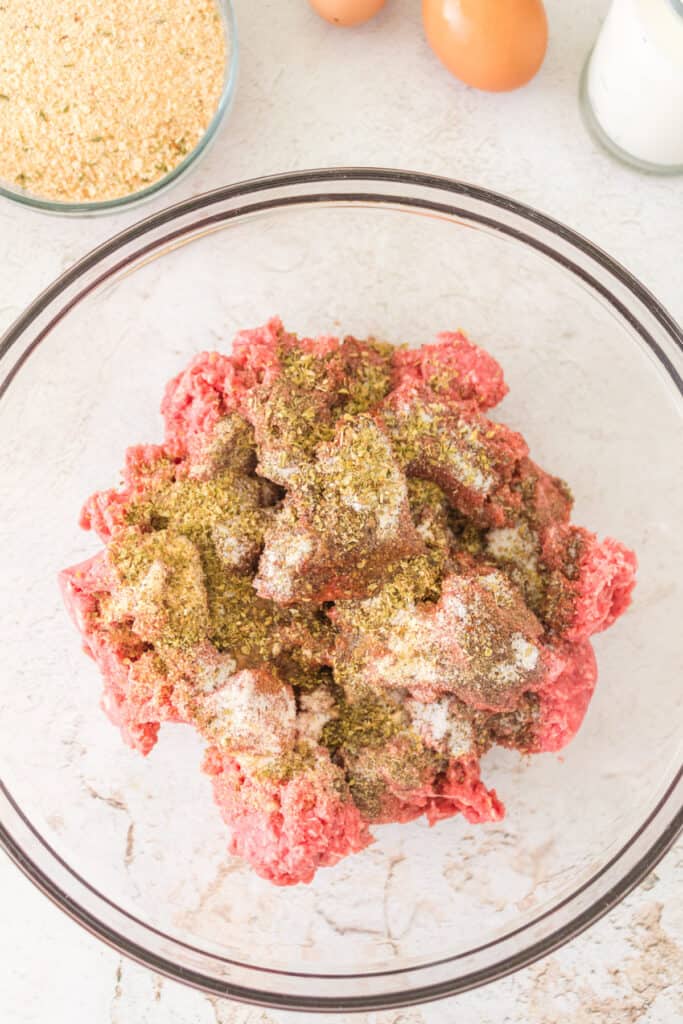 	Seasonings sprinkled over ground beef in a glass mixing bowl