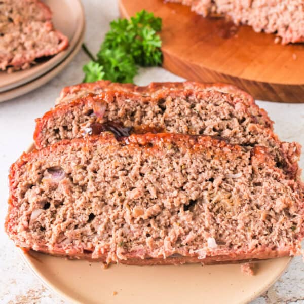 Three thick slices of smoked meatloaf on a plate with fresh parsley garnish