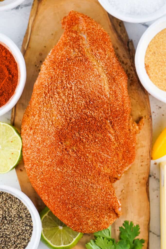 Seasoned raw turkey breast surrounded by spices and lime on a wooden board