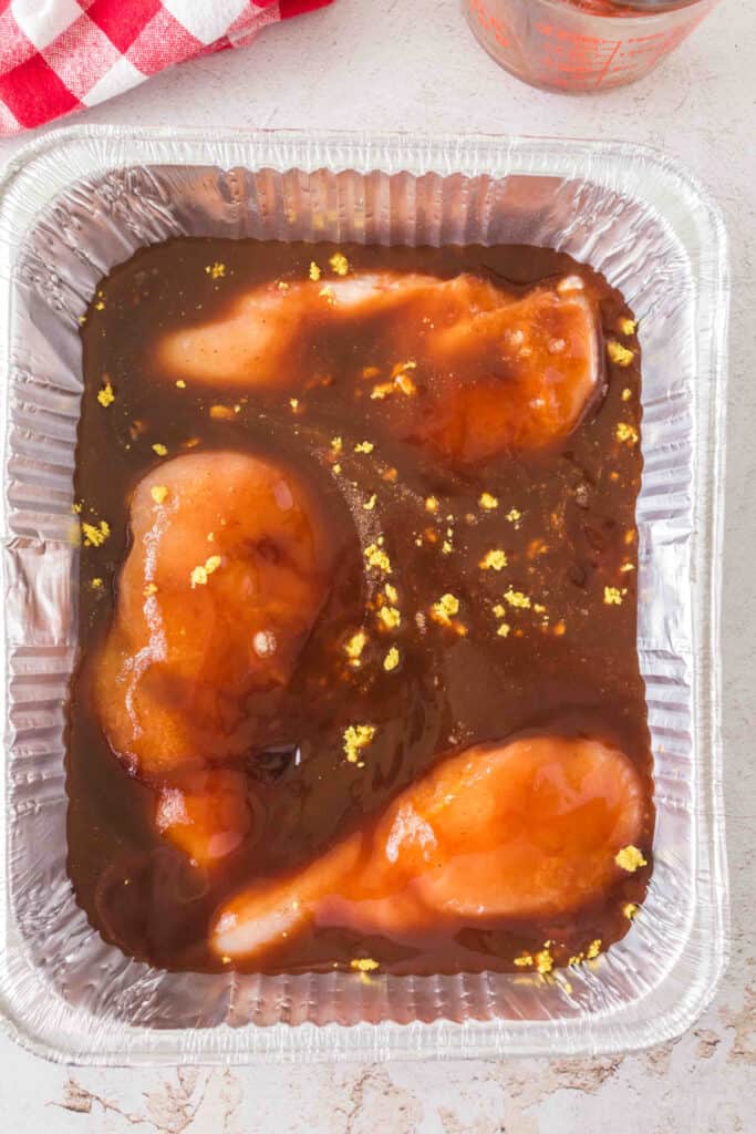 Chicken breasts in an aluminum pan topped with spices and crumbled bouillon.