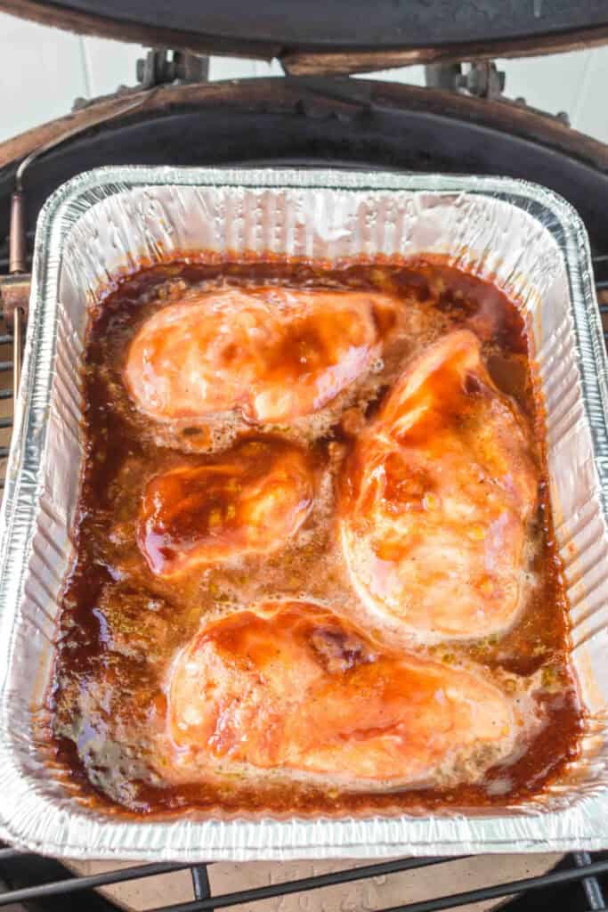 Chicken breasts simmering in sauce inside a smoker, partially caramelized.