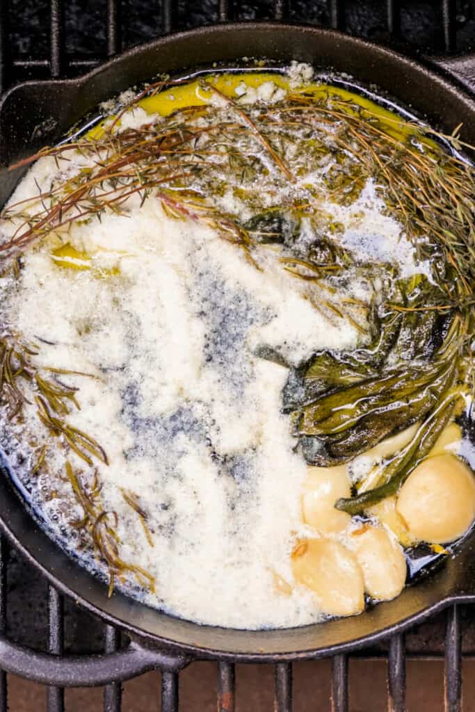 Melted butter infused with herbs and garlic simmering in a cast iron pan