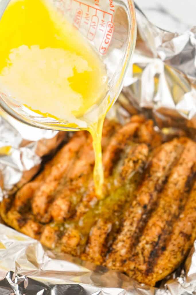 Melted butter being poured over smoked turkey breast in a foil wrap