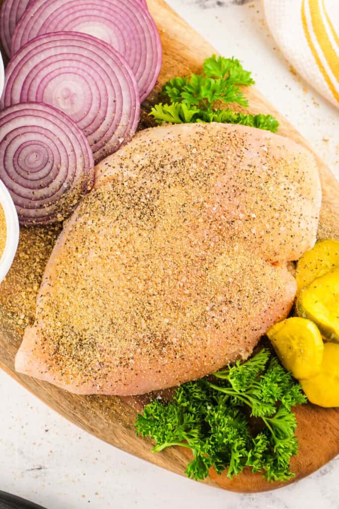 Raw seasoned turkey breast on a cutting board with red onion slices and fresh parsley